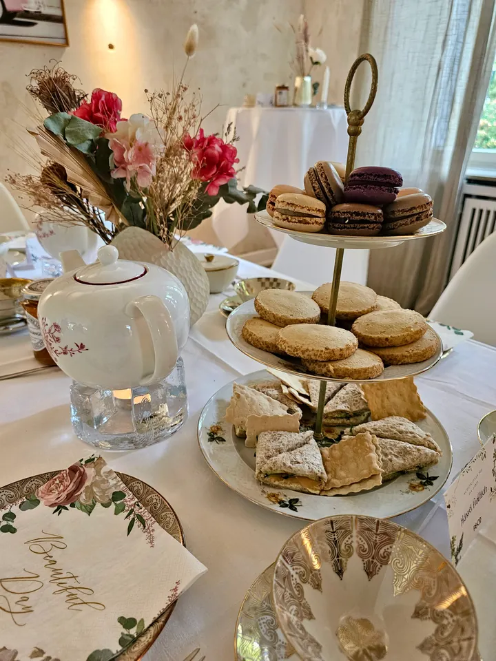 A festive tea table with a teapot, macarons, pastries and sandwiches on a tiered stand
