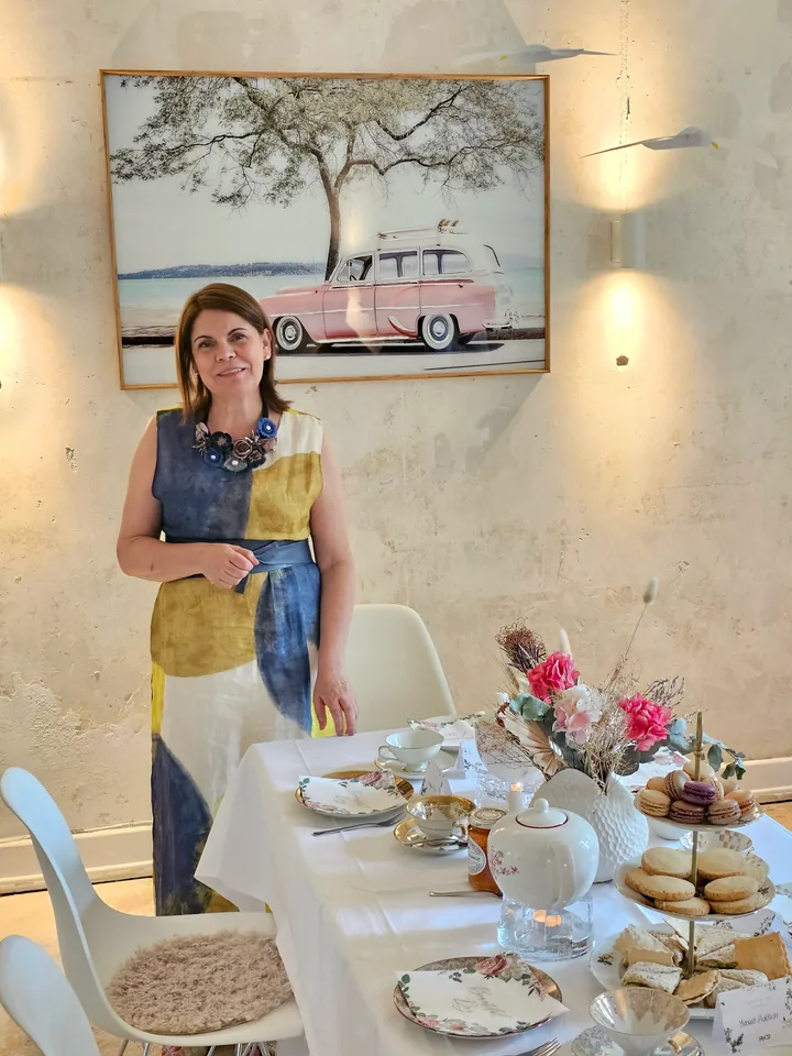 Maria Moreno beside a lovingly set tea table with porcelain, pastries and flowers in the tea room