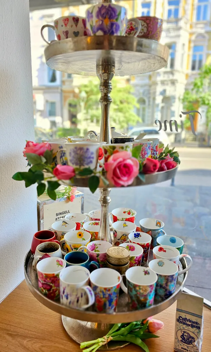 Tazas de porcelana floral y rosas rosas en una bandeja de varios pisos junto a la ventana del salón