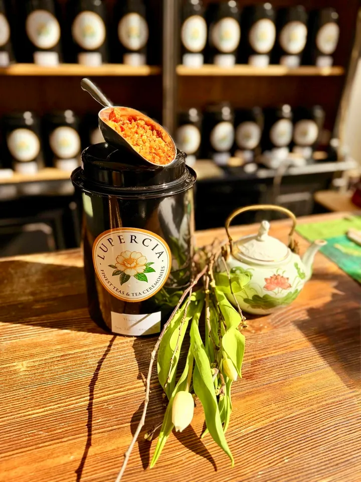 Una lata de té Lupercia con una cucharada de infusión de frutas, una tetera floral y una rama de magnolia