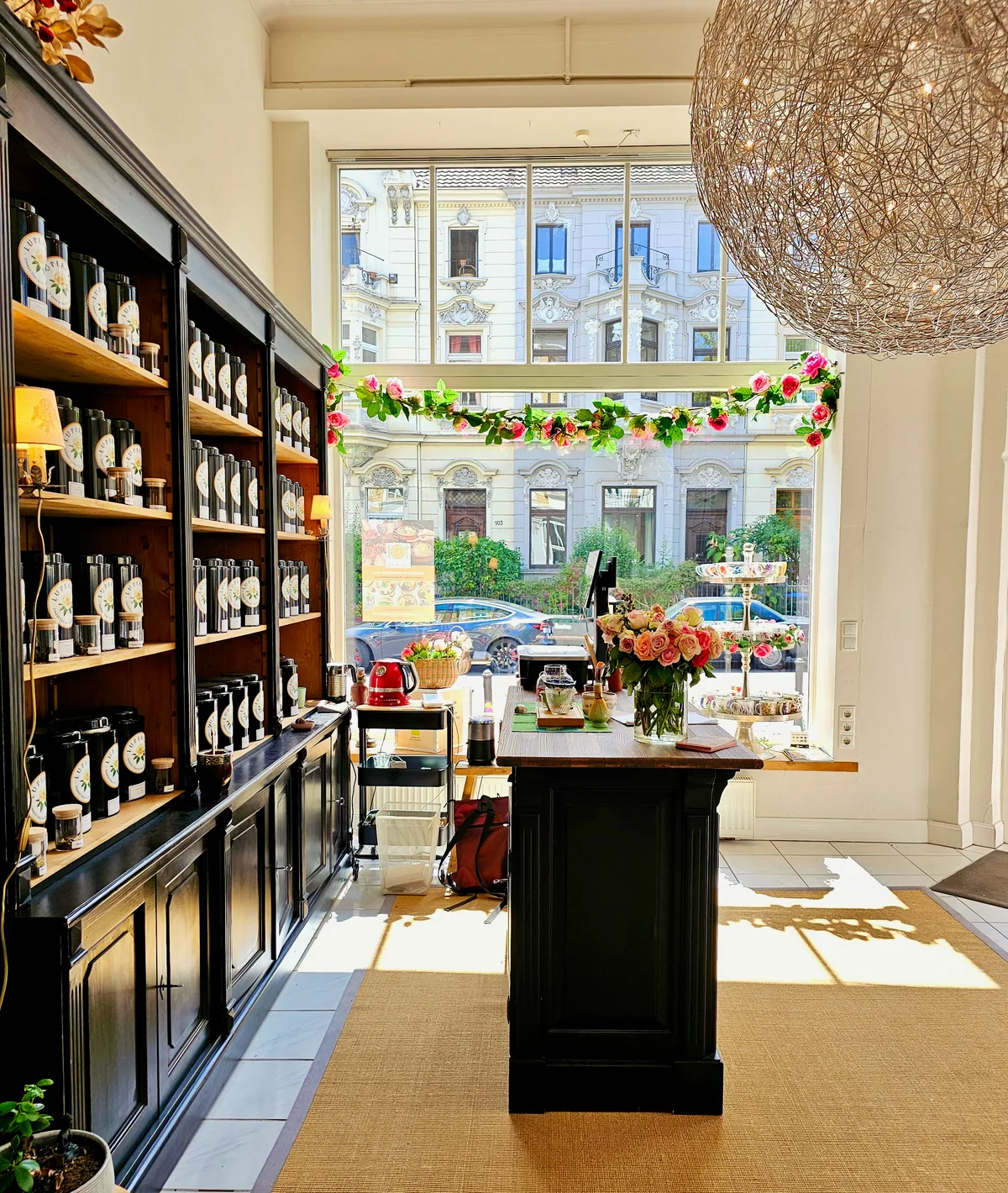 Sunlight in the Lupercia tea room, with tea shelves, flowers and views of Bonn’s Südstadt