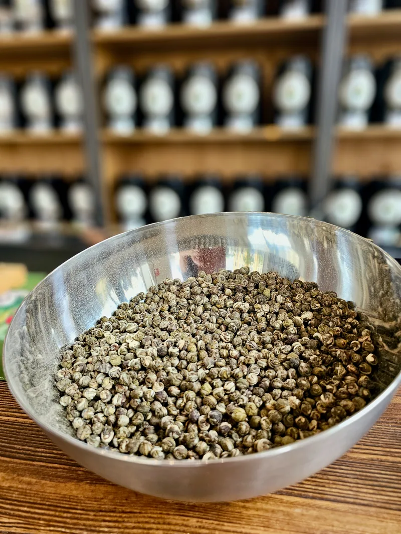 Perlas de té finamente enrolladas en un cuenco plateado ante las estanterías de té de Maria