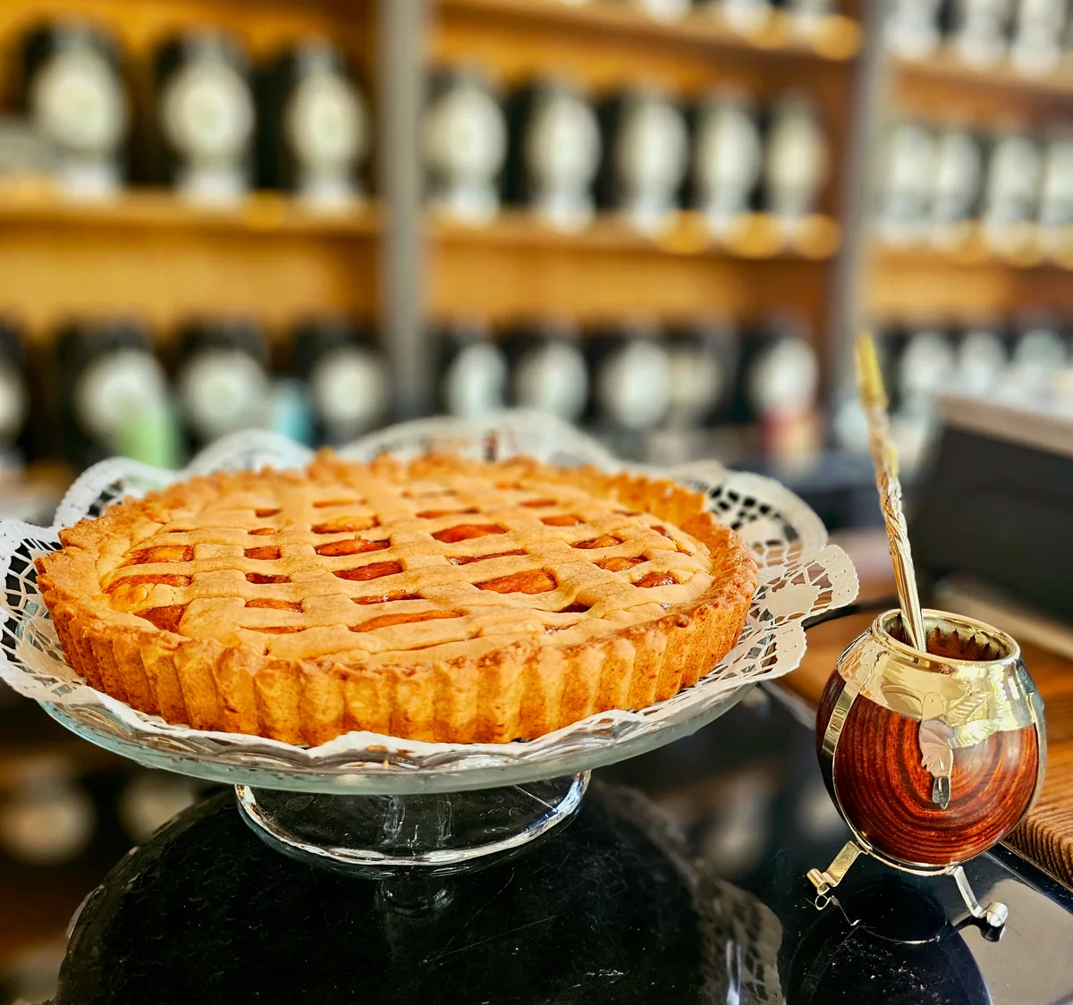 A golden-brown lattice cake on a glass plate beside a traditional mate gourd with a bombilla