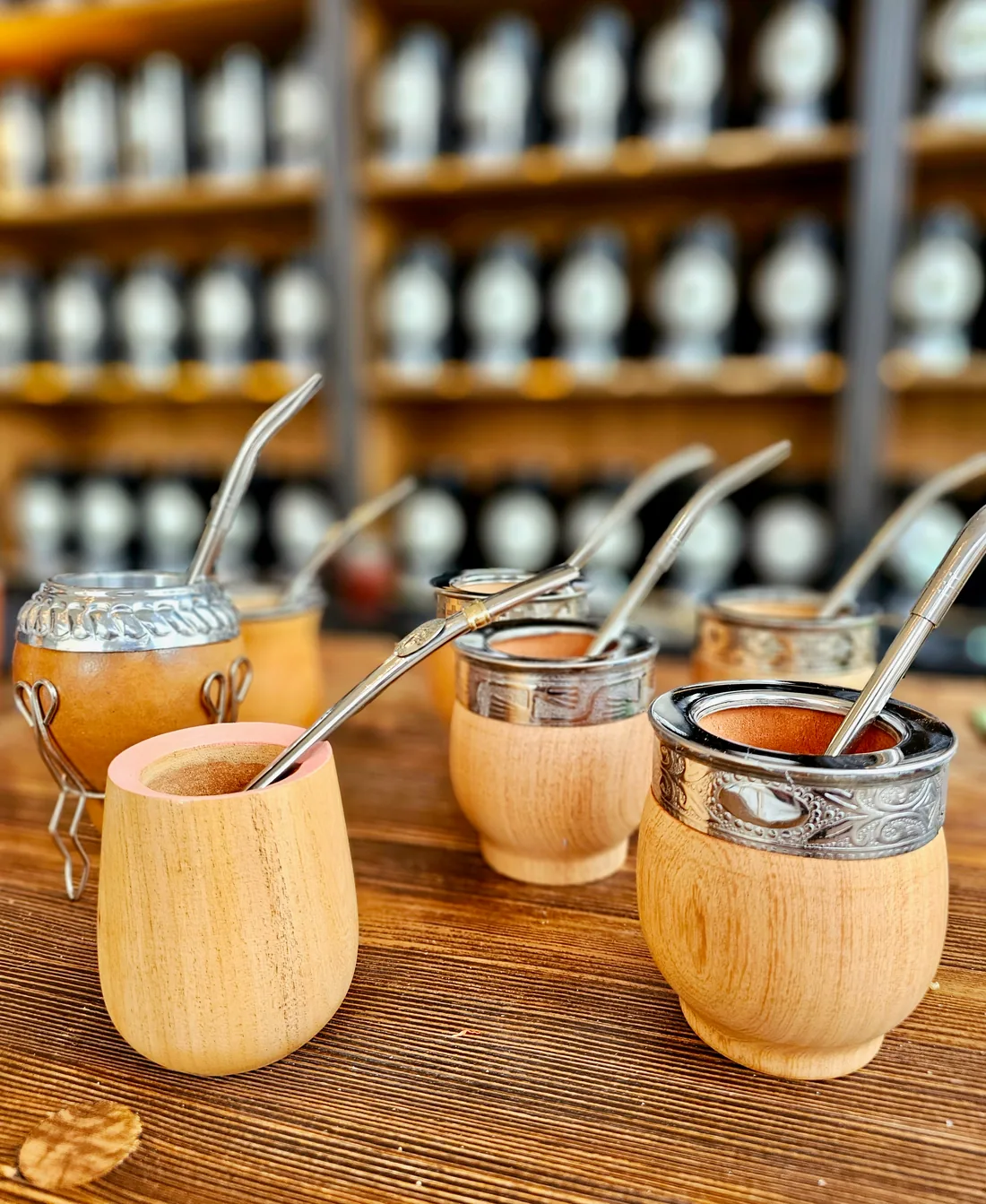 A selection of wooden mate gourds with decorated metal rims and silver-coloured bombillas in front of Maria’s tea shelves