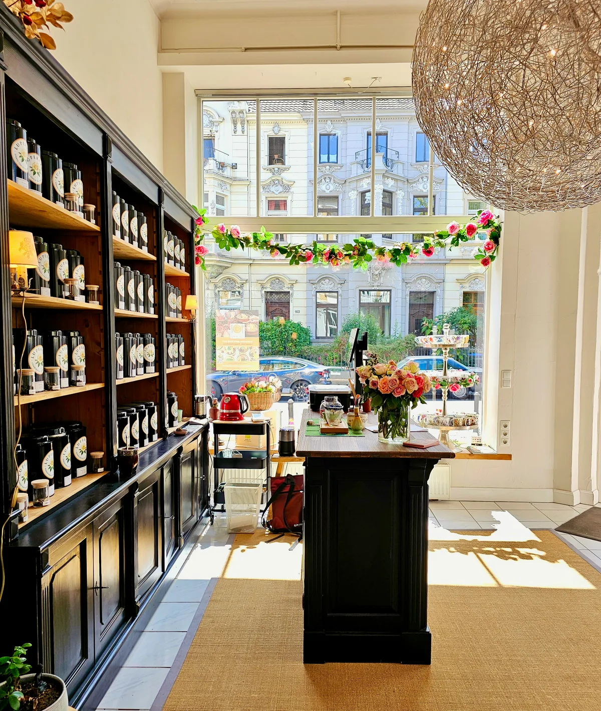 The sunlit Lupercia tea room with dark tea shelves, flowers and a large window onto Bonn’s Südstadt