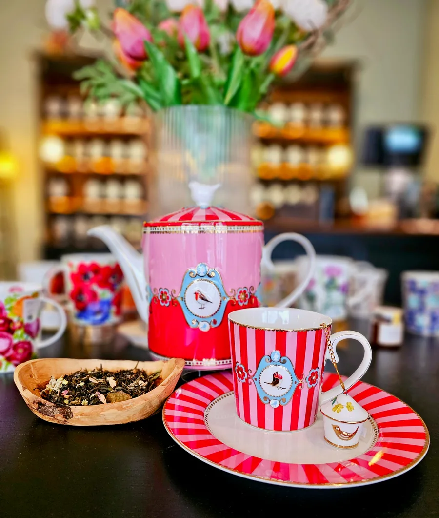 A pink and red striped teapot with a matching cup and a wooden bowl of loose tea