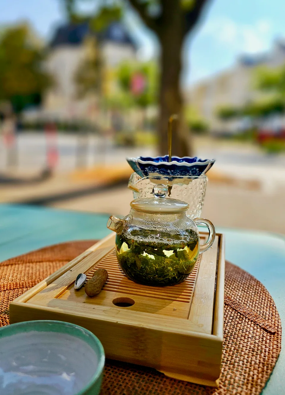 Hojas de té verde abriéndose en una tetera de cristal sobre una bandeja de bambú junto a la ventana de Lupercia