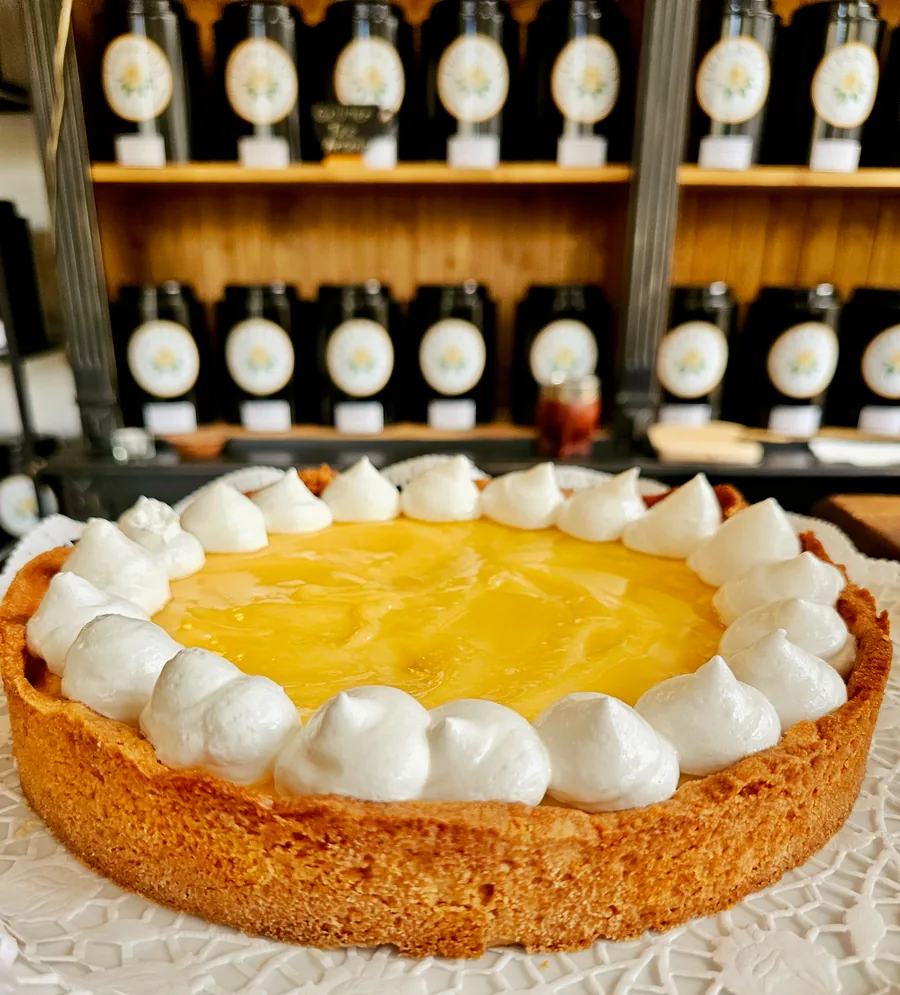 Una tarta dorada con decoración blanca de manga pastelera ante las estanterías de té de Lupercia