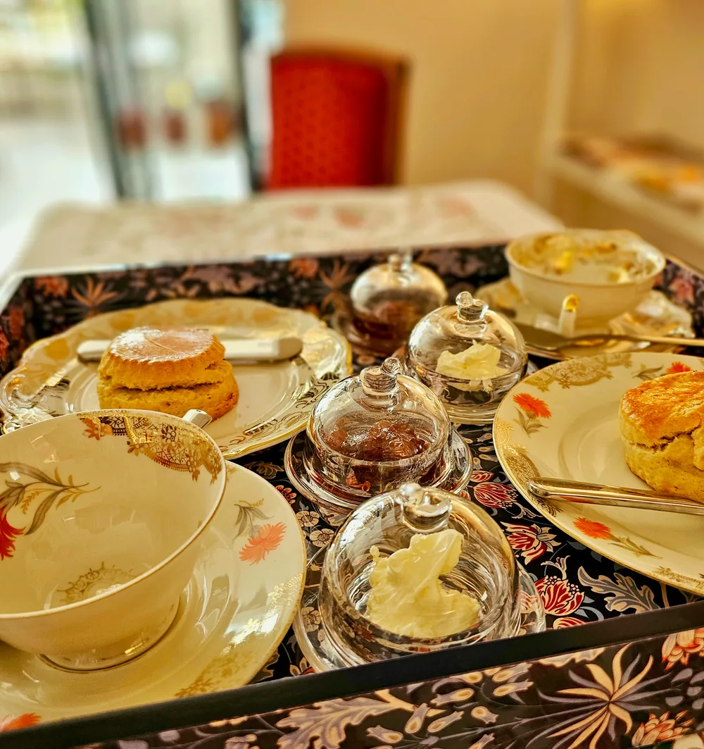 Una bandeja preparada con scones, clotted cream, mermelada y porcelana floral fina