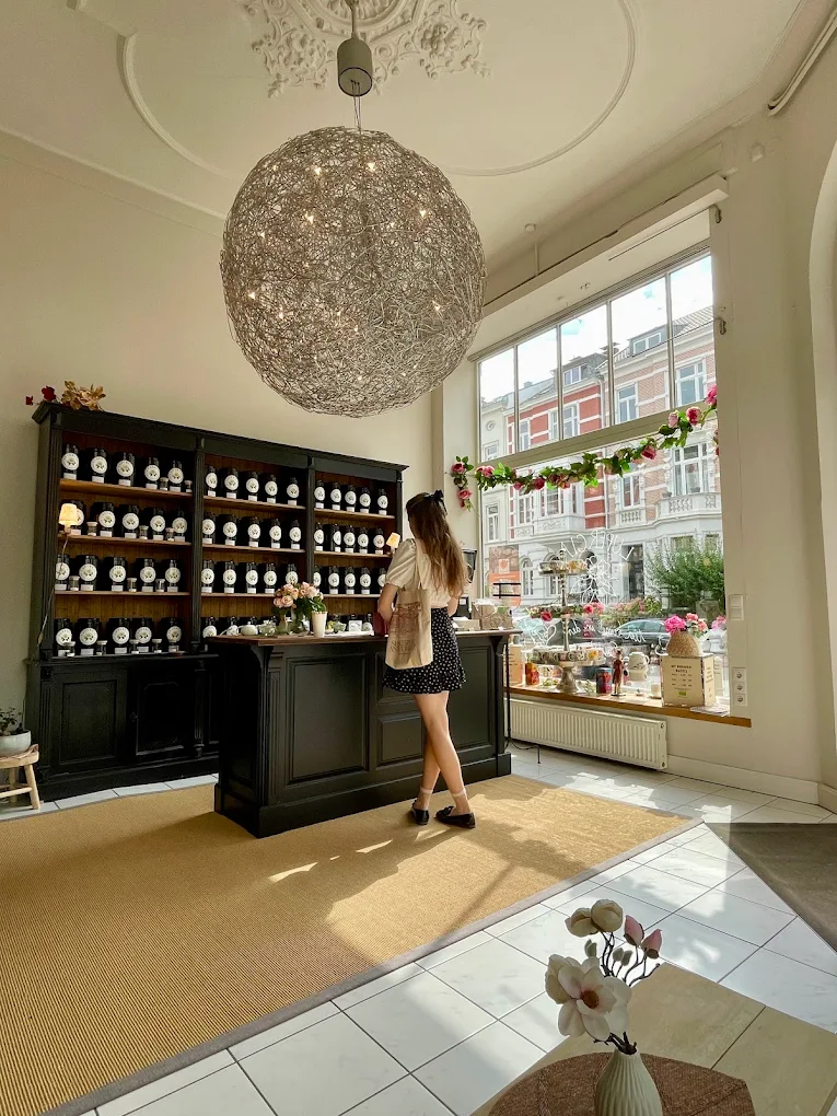 Eine Kundin am schwarzen Apothekentresen des Lupercia-Salons unter skulpturalem Lüster und historischer Stuckdecke, Blick durchs Schaufenster auf die gründerzeitlichen Bonner Fassaden