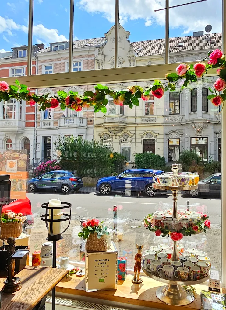 Vintage-Porzellantassen auf Etagere im Schaufenster mit Rosen-Girlande und Blick auf die gründerzeitlichen Bonner Fassaden