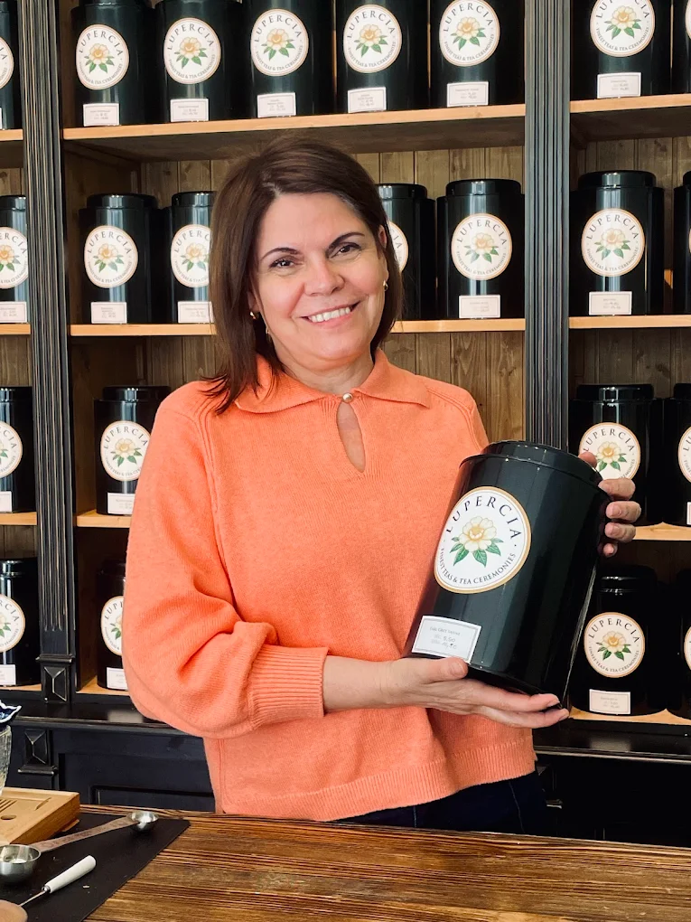 Maria Moreno, Gründerin von Lupercia, mit handsignierter Lupercia-Teedose vor der Wand mit über 70 Teesorten